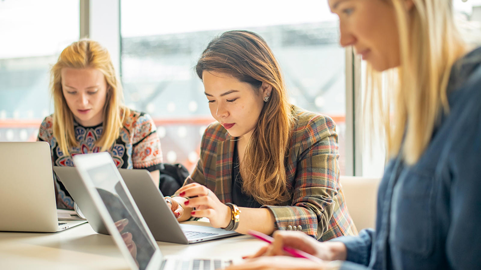three students sitting at a table using laptops
